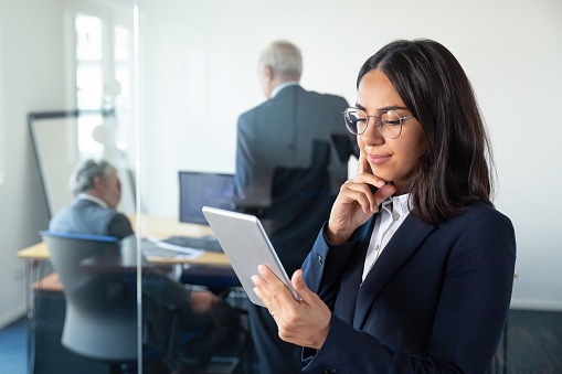Pensive female manager in glasses looking on tablet screen